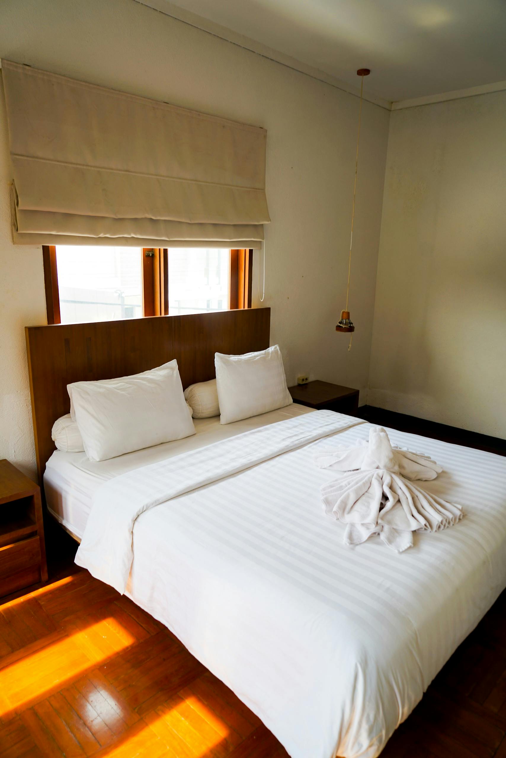Bright minimalist bedroom featuring white linens and decorative towel arrangement on a wooden floor.